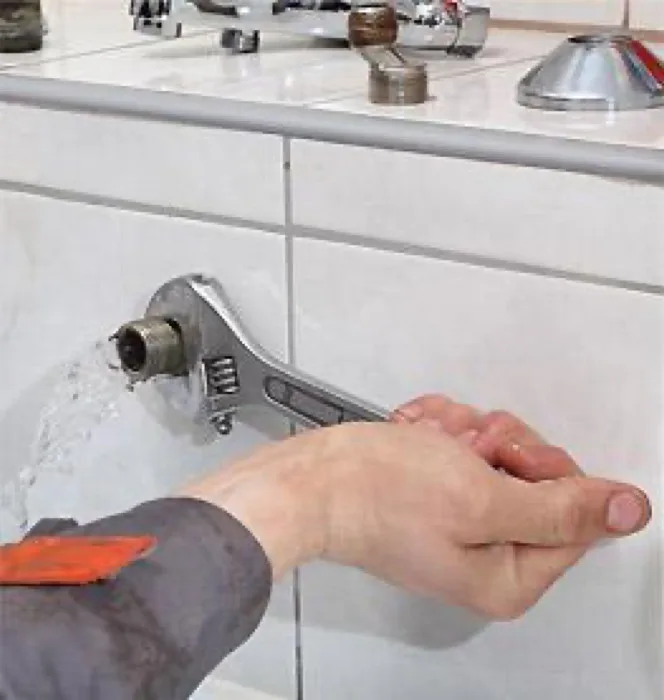 Plumber repairing a kitchen faucet with a wrench