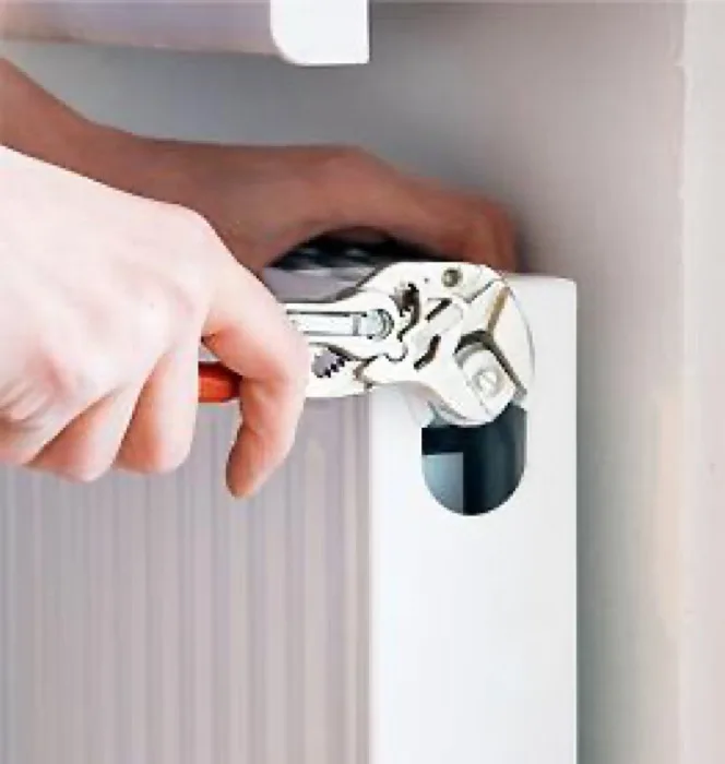 Technician using a wrench to service a home heating radiator